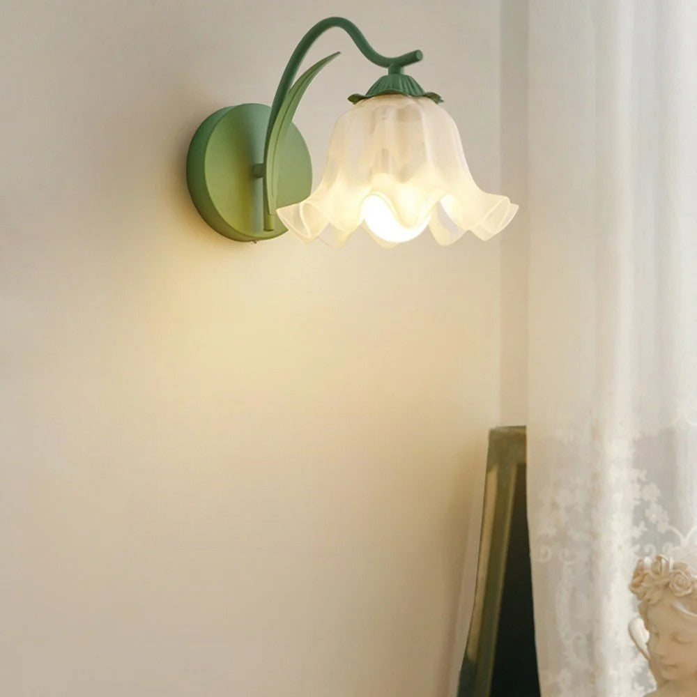 Green French flower sconce with wavy glass shade, softly illuminating a cozy bedroom corner near sheer curtains.