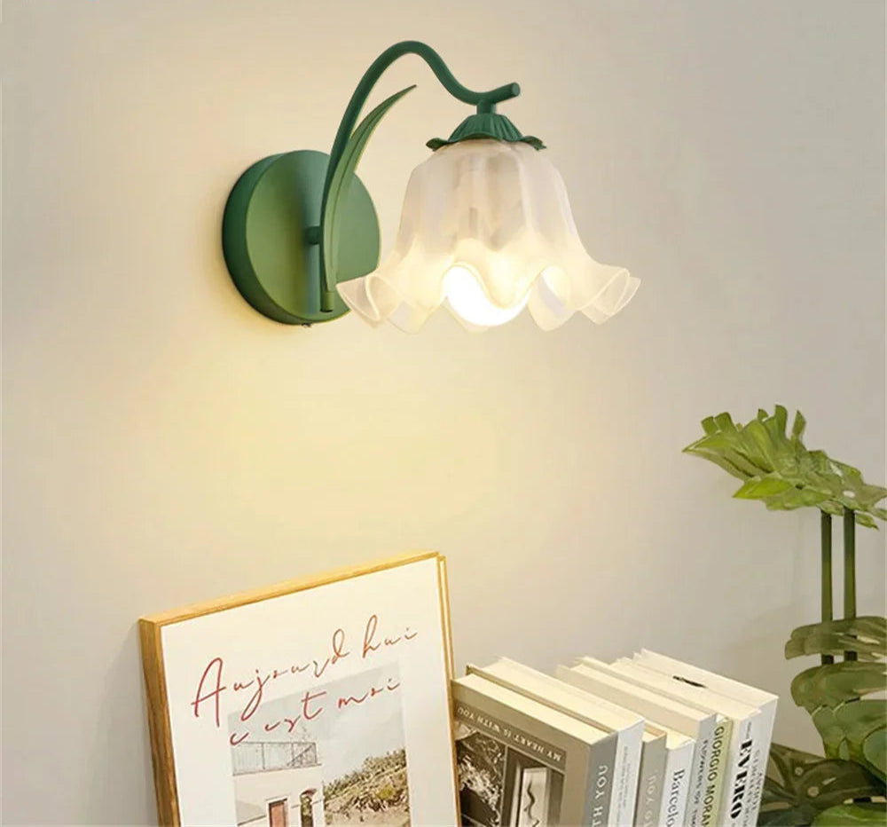 French flower sconce in green with frosted glass shade, mounted on wall above books and decor, ideal for modern bedroom lighting.