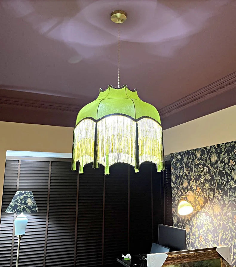 Luxury French velvet chandelier glowing in a dark room, highlighting its green fabric and golden tassel details.