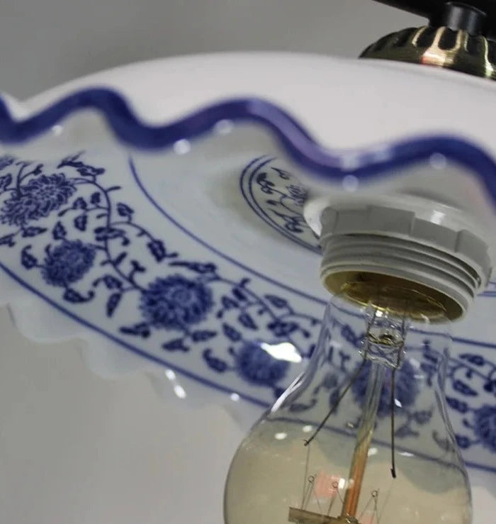 Close-up of scalloped ceramic pendant light with blue floral pattern and LED bulb, showcasing intricate design details.