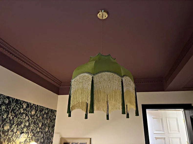 Vintage green pendant light with yellow fringe, hanging in a richly colored room with classic wall patterns.