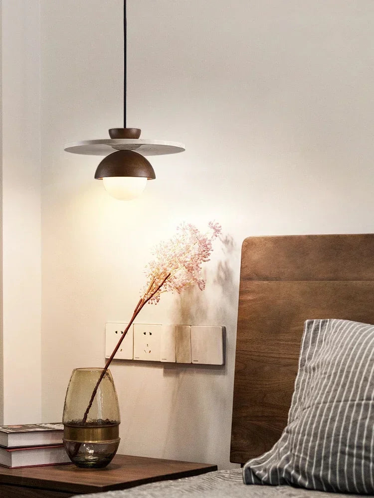 Modern walnut wood pendant light with stone disc above bedside table, perfect for warm ambient bedroom lighting.