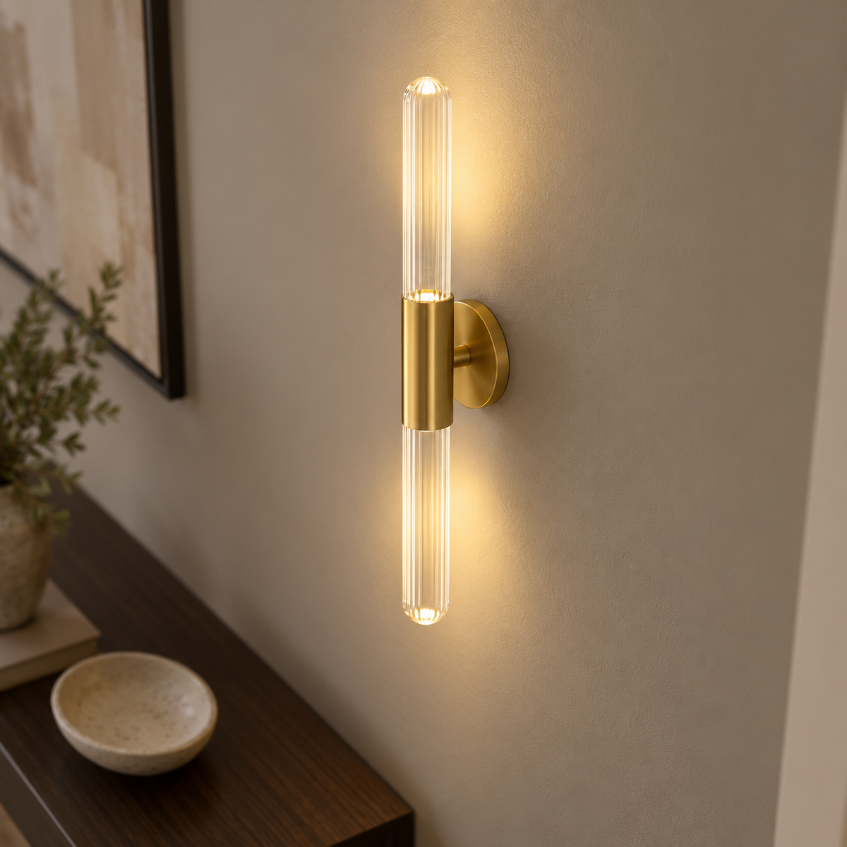 Above-angle photograph of a clear glass rod LED wall light with gold fitting