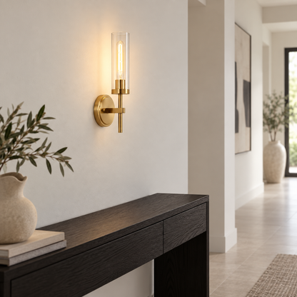 Gold clear glass cylinder wall lamp installed above a dark console
