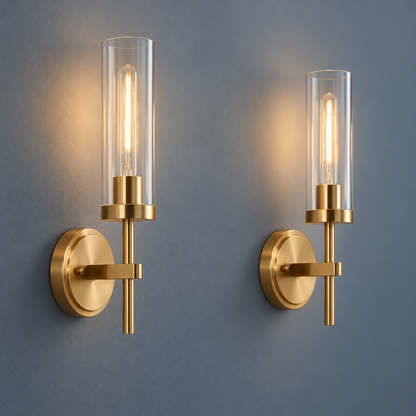 Pair of gold clear glass cylinder wall lights installed on a smooth gray wall