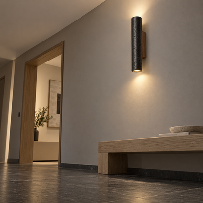 Low-angle view of a black travertine wall lamp installed above a minimalist hallway bench