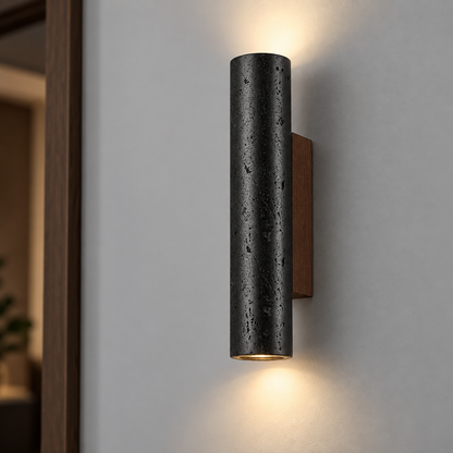 Black round travertine wall light in the 32 cm size, centered on a smooth gray wall
