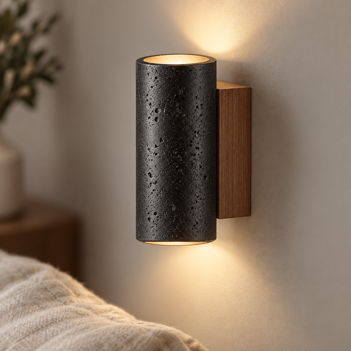 Black round travertine wall light, 16 cm high, installed on a smooth gray wall