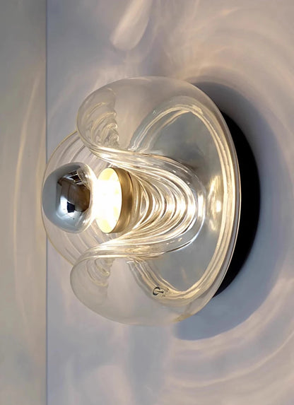 Angled view of designer glass wall sconce with LED light, featuring artistic curves and warm illumination.