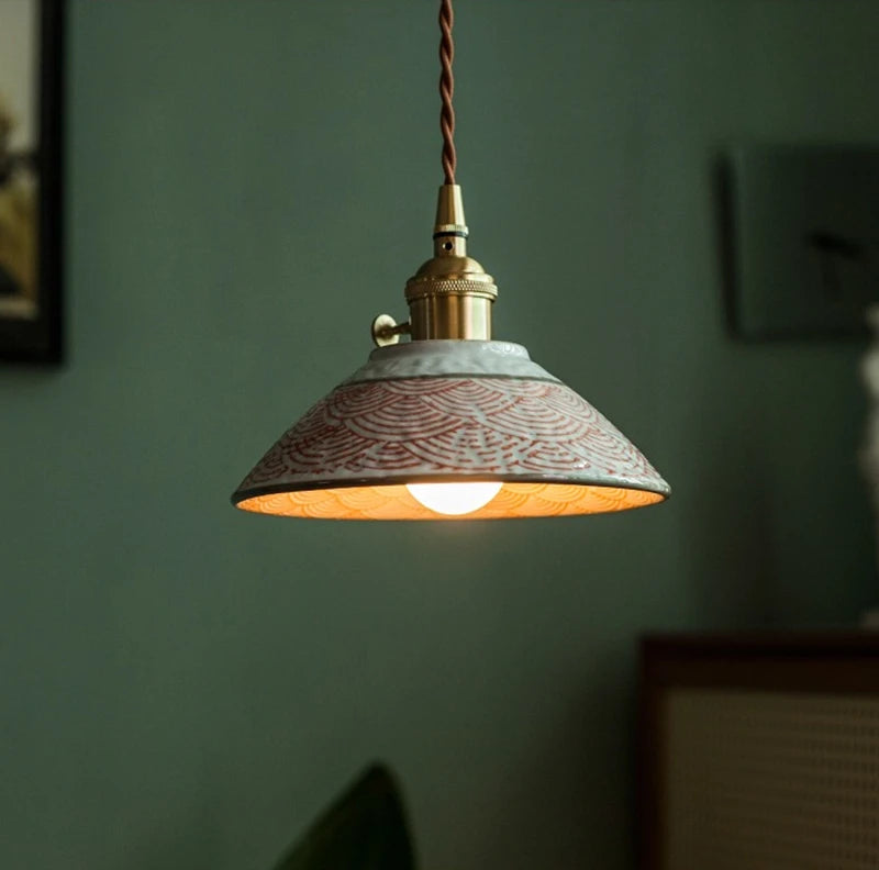 Close-up of red wave-patterned ceramic pendant lamp with LED bulb and brass fixture, perfect for modern interiors.