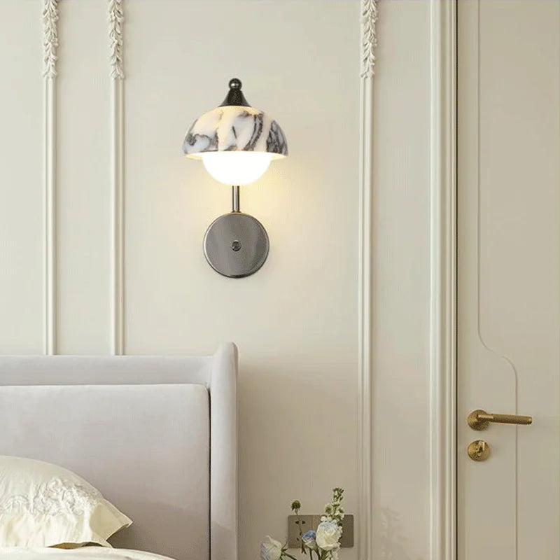 Alabaster wall sconce installed beside a bed in a modern bedroom, providing soft ambient lighting with elegant black stone design.
