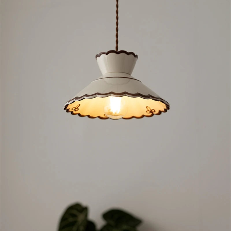 White ceramic pendant light with scalloped edges and LED bulb, casting warm glow in a minimalist room.