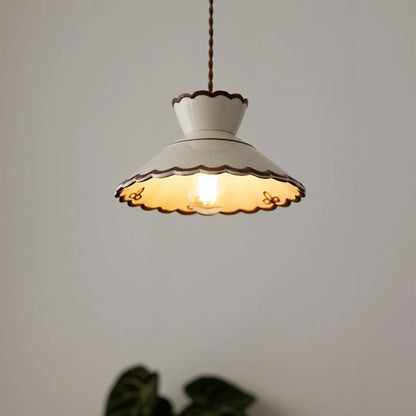 White ceramic pendant light with scalloped edges and LED bulb, casting warm glow in a minimalist room.