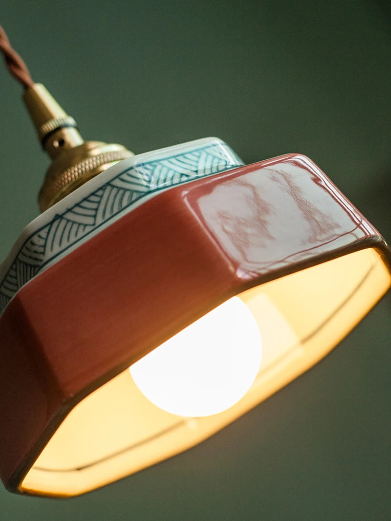 Close-up of vintage ceramic pendant lamp with LED bulb and copper fixture, showcasing hand-painted geometric detailing.