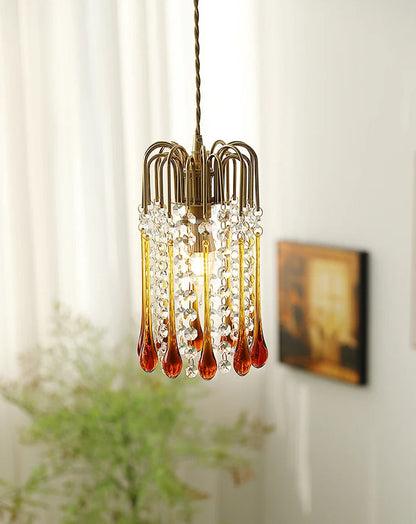 Elegant vintage chandelier with amber glass drops and crystal accents, suspended in a softly lit bedroom setting.