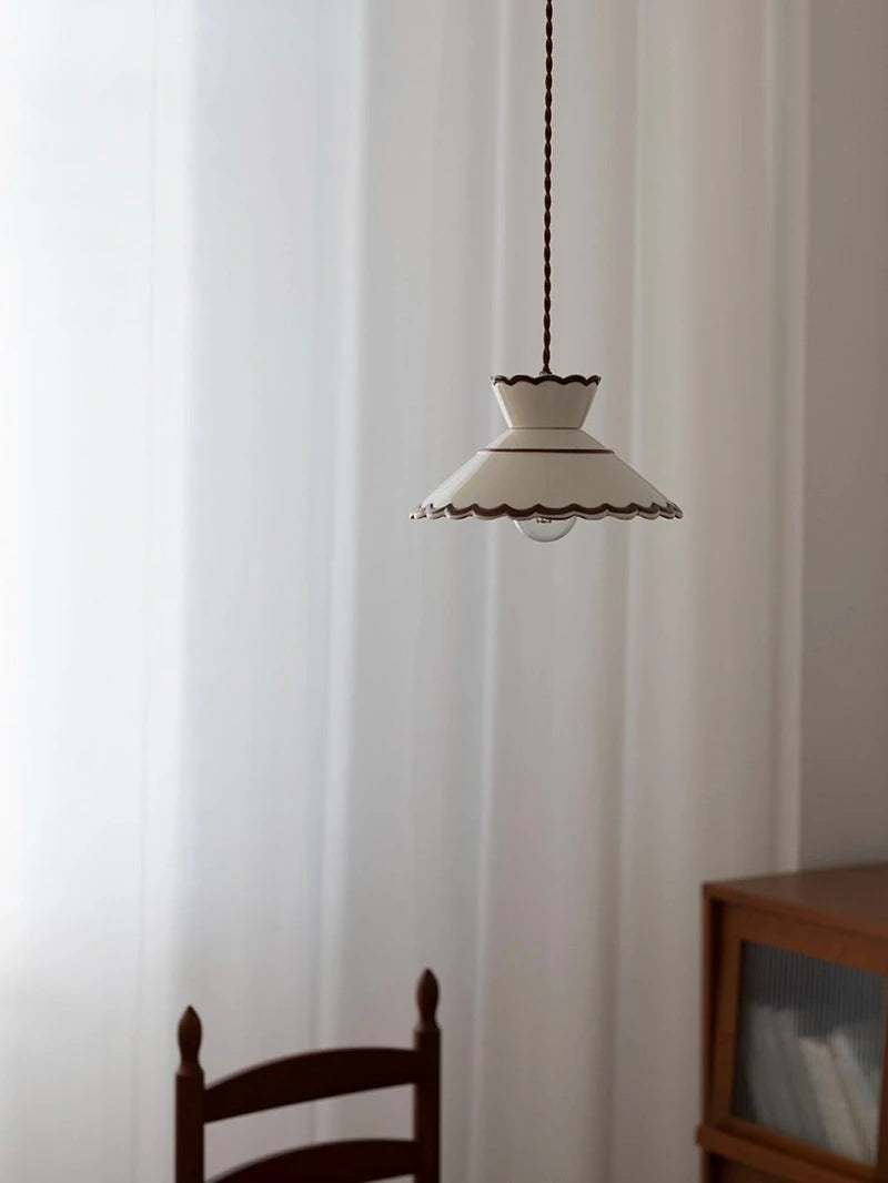 Bottom view of scalloped ceramic pendant lamp with LED bulb, showing warm glow and decorative cutouts.