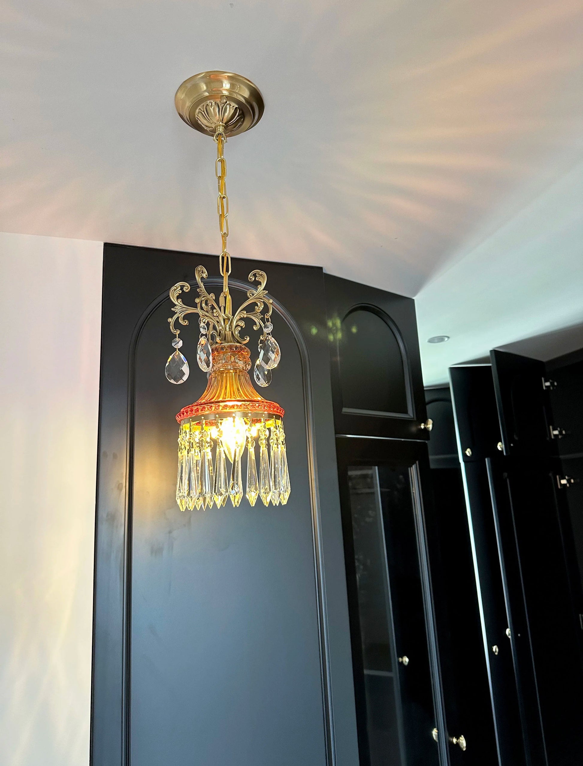 Luxury French crystal chandelier with warm glow, retro pendant light enhancing black paneled room décor.