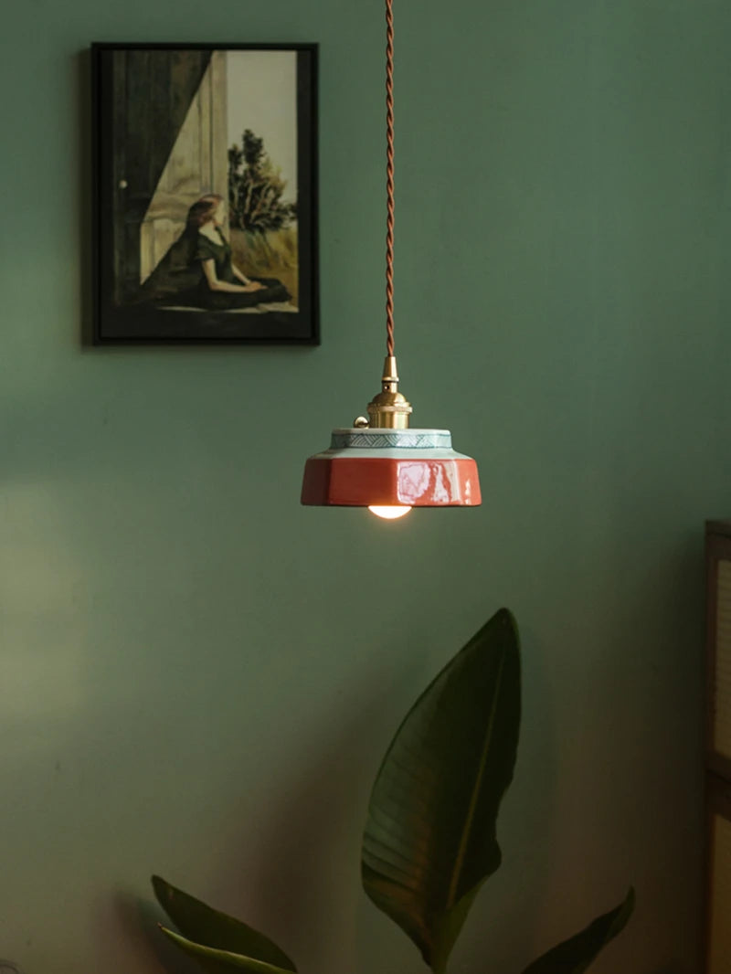 Freehand painted ceramic pendant lamp with LED lighting, suspended above a plant in a cozy, modern room setting.