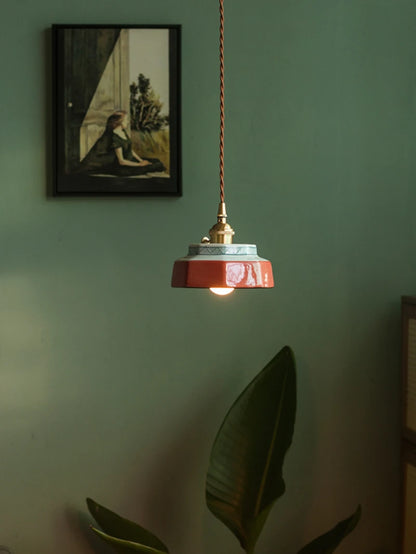 Freehand painted ceramic pendant lamp with LED lighting, suspended above a plant in a cozy, modern room setting.