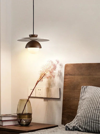 Modern walnut wood pendant light with stone disc above bedside table, perfect for warm ambient bedroom lighting.