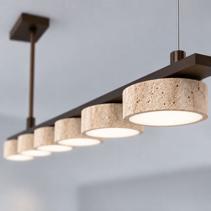 Close-up of illuminated shallow beige travertine puck shade on six-head bronze linear pendant