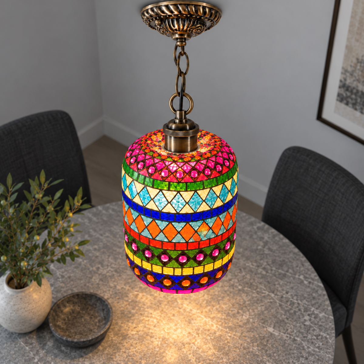 Illuminated Style B mosaic cylinder pendant with bronze chain, presented from an elevated side angle in a neutral grey room.