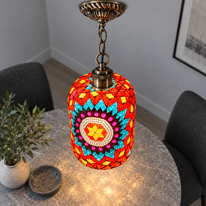 Illuminated Style D mosaic cylinder pendant with bronze chain, presented from an elevated side angle in a neutral grey room.