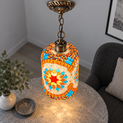 Illuminated Style E mosaic cylinder pendant with bronze chain, presented from an elevated side angle in a neutral grey room.