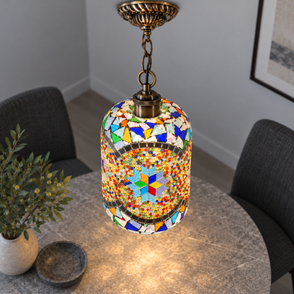Illuminated Style F mosaic cylinder pendant with bronze chain, presented from an elevated side angle in a neutral grey room.