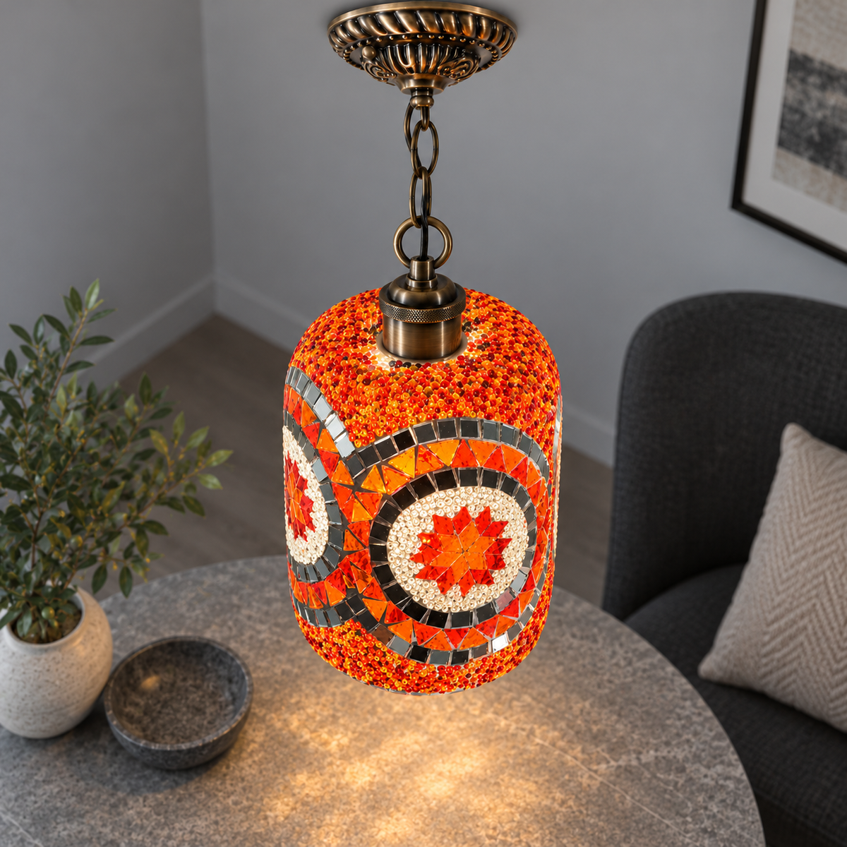 Illuminated Style G mosaic cylinder pendant with bronze chain, presented from an elevated side angle in a neutral grey room.