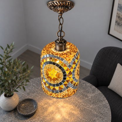 Illuminated Style I mosaic cylinder pendant with bronze chain, presented from an elevated side angle in a neutral grey room.