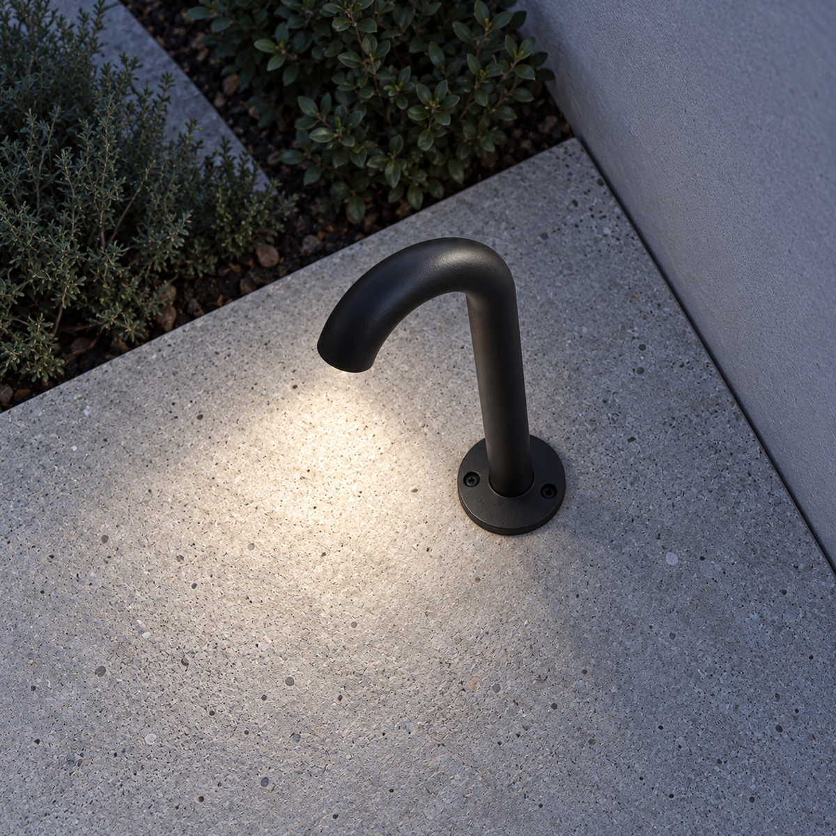 Above view of an illuminated black round-base curved path light bolted to a grey terrace, with light pool visible
