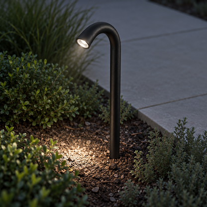 Black ground-spike curved aluminium path light illuminated in a border, elevated opposite-side commercial view