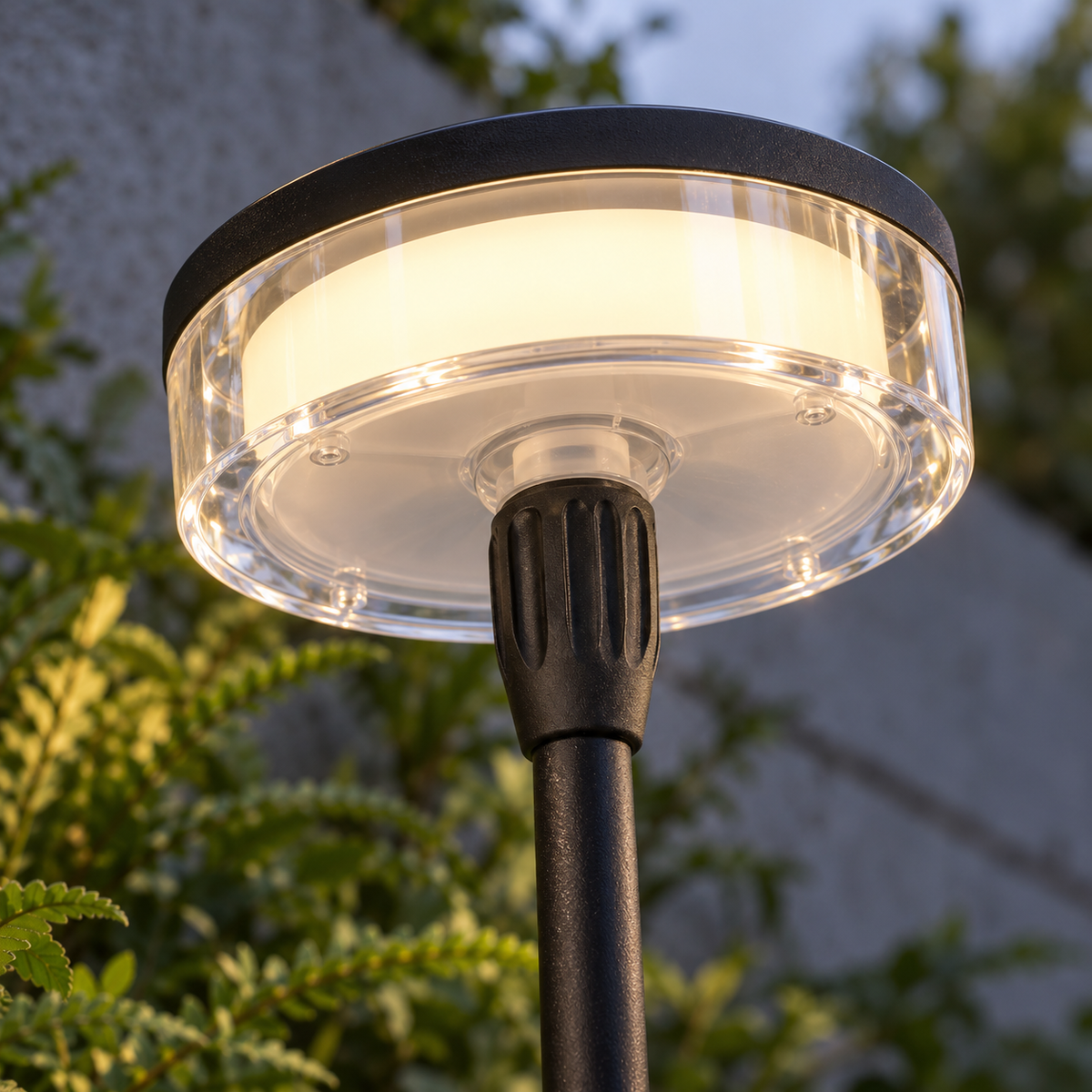 Low underside close-up of the illuminated solar disc diffuser, mounting socket and black stem in a garden border