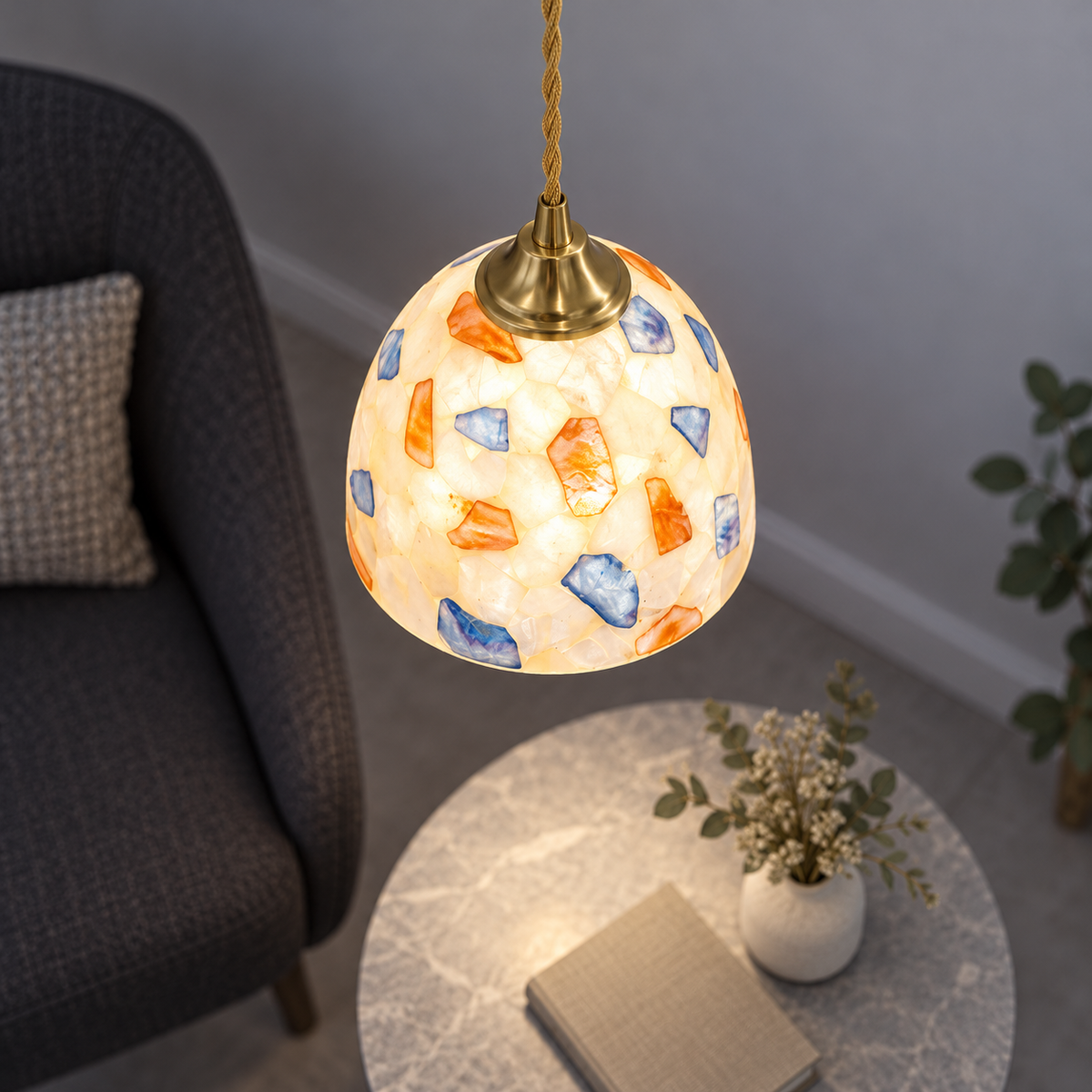 Lit multicolour shell dome pendant centred in a neutral grey nook, photographed from a useful elevated side angle.