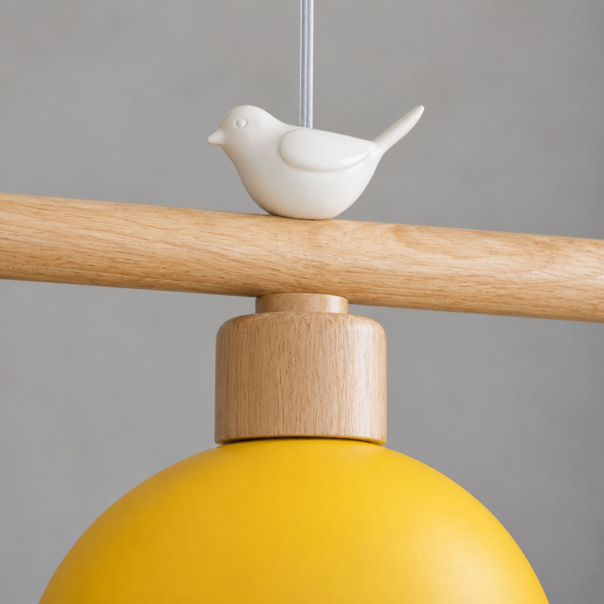 Close-up of the white bird ornament, round wood bar and yellow metal shade of the woodland bird pendant